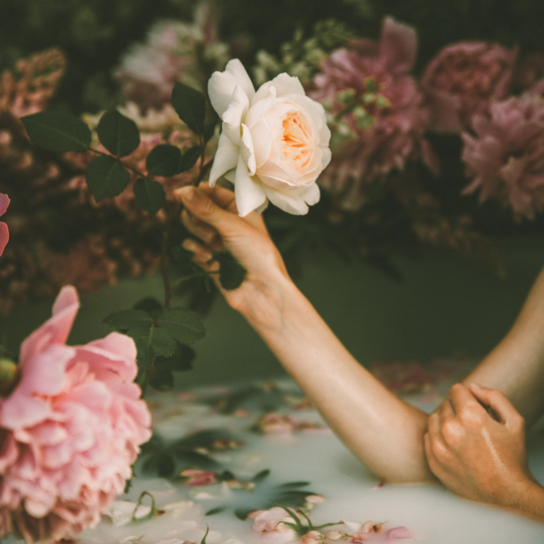 Image is of a lady sitting in a milk bath surrounded by blooms